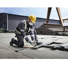 Muž s ochrannou helmou a maskou reže kov uhlovou brúskou, pričom lietajú iskry.