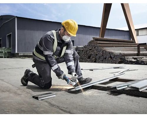Muž s ochrannou helmou a maskou reže kov uhlovou brúskou, pričom lietajú iskry.