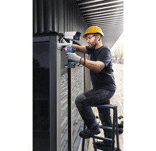 Muž montuje bezpečnostnú kameru na budovu pomocou akumulátorového skrutkovača.