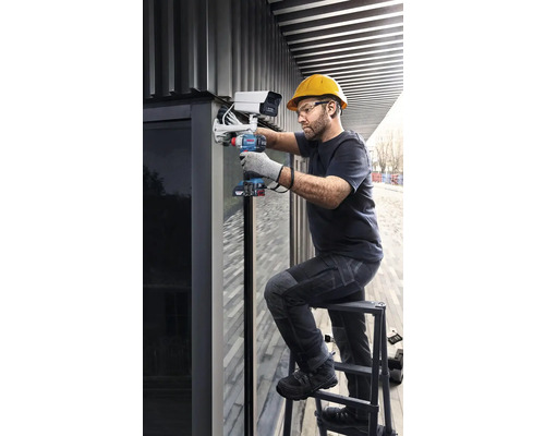 Muž montuje bezpečnostnú kameru na budovu pomocou akumulátorového skrutkovača.