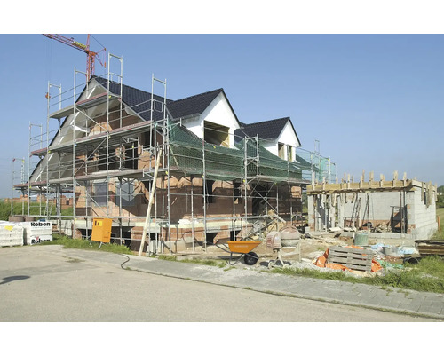 Nová stavba domu s lešením, miešačkou cementu a stavebnými materiálmi.