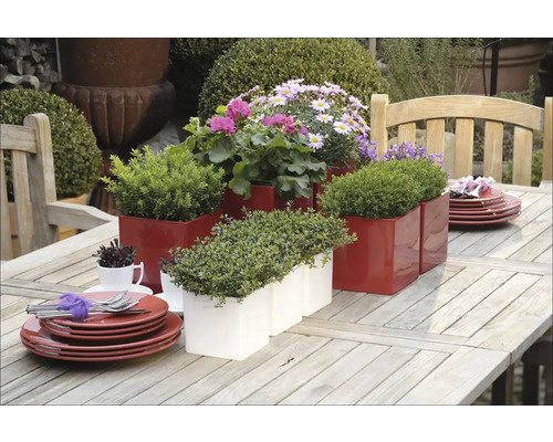 Dekoratívny záhradný stôl s červenými a bielymi kvetináčmi a riadom.