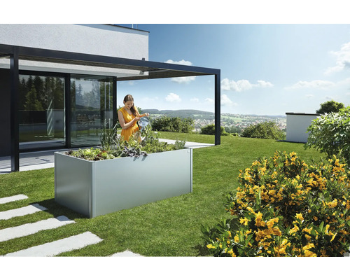 Žena zalieva rastliny vo vyvýšenom záhone v záhrade vedľa domu.