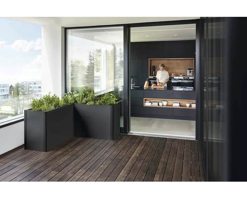 Balkónová scéna s kvetináčmi a otvorenou kuchyňou so ženou pripravujúcou jedlo.