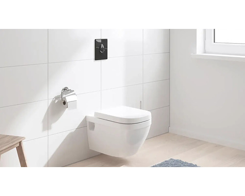 Závesné WC s ovládacou doskou a držiakom toaletného papiera v kúpeľni s bielymi obkladmi.