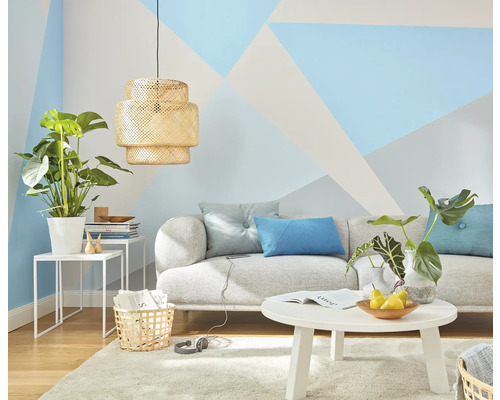 Obývacia izba s pohovkou, stolom, lampou a izbovými rastlinami pred stenou s geometrickými vzormi