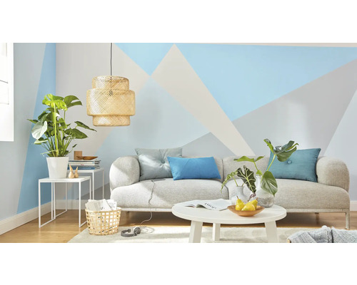 Obývacia izba s pohovkou, stolom, lampou a izbovými rastlinami pred stenou s geometrickými vzormi