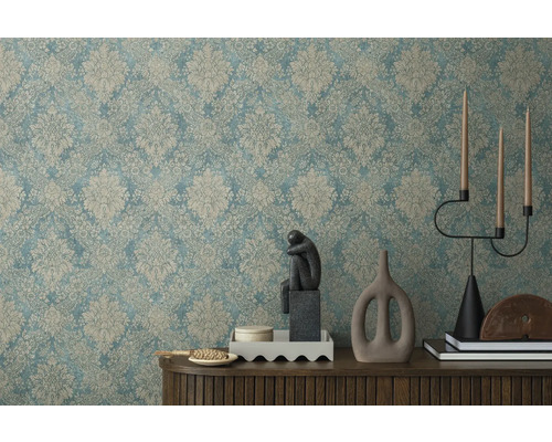 Dekoratívny interiér so vzorovanou tapetou, skulptúrou, svietnikom a dekoratívnymi prvkami na drevenej skrinke.