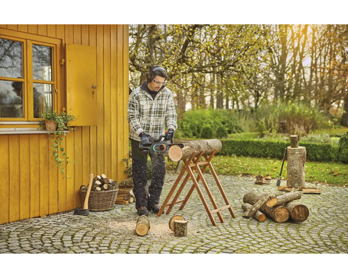 Muž pília drevo motorovou pílou v záhrade.