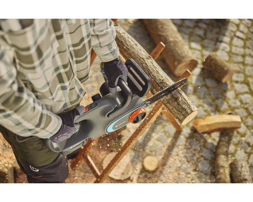 Muž pília drevo akumulátorovou pílou Gardena.