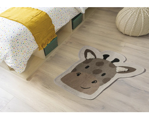 Izbová scéna s posteľou, sedákom a kobercom v tvare hlavy žirafy.