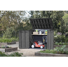 Záhradná skriňa s otvoreným vekom a dverami v záhrade, s kosačkou na trávu a záhradným náradím