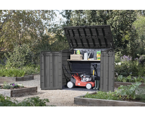 Záhradná skriňa s otvoreným vekom a dverami v záhrade, s kosačkou na trávu a záhradným náradím