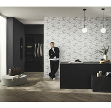 Pohľad na izbu s tapetou so vzorom, komodou, osvetlením a mužom