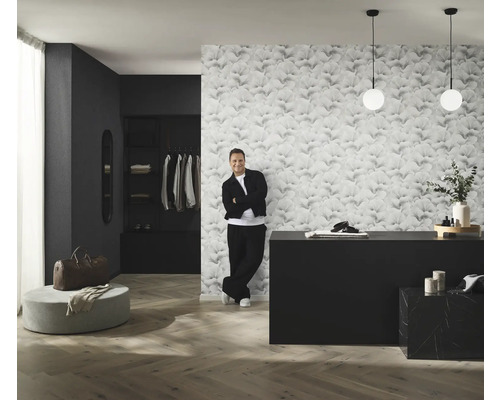 Pohľad na izbu s tapetou so vzorom, komodou, osvetlením a mužom