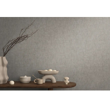 Dekoratívne zátišie s vázou, misou a okrasnými predmetmi na drevenom stole pred sivou stenou.