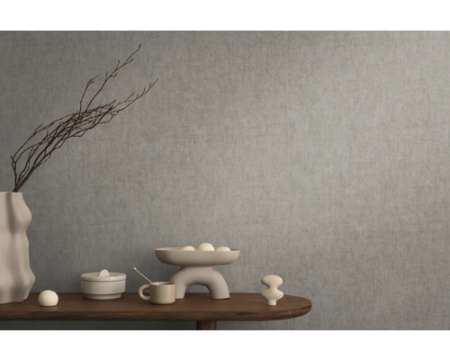 Dekoratívne zátišie s vázou, misou a okrasnými predmetmi na drevenom stole pred sivou stenou.