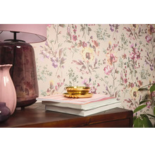 Interiérová scéna s kvetinovou tapetou, stolnou lampou, vázami, knihami a miskou.