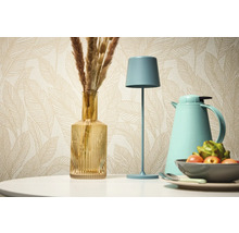 Dekoratívne zátišie so stolnou lampou, vázou a termoskou na pozadí vzorovanej tapety.