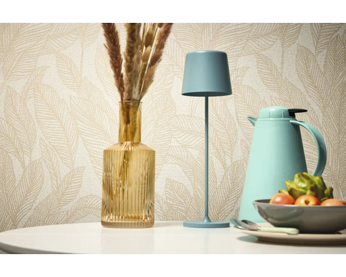 Dekoratívne zátišie so stolnou lampou, vázou a termoskou na pozadí vzorovanej tapety.