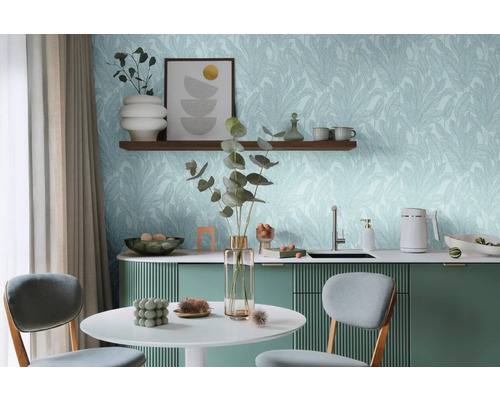 Svetlá miestnosť so stolom, stoličkami a kuchynským kútom pred stenou s tapetou s motívom listov.
