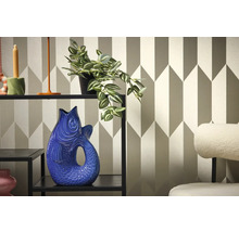 Dekoratívny interiér s policou, rastlinou a vázou v tvare ryby na pozadí geometrickej tapety.