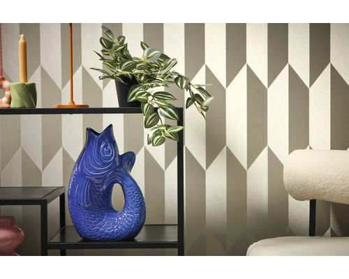 Dekoratívny interiér s policou, rastlinou a vázou v tvare ryby na pozadí geometrickej tapety.