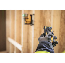 Ruka v rukavici drží diaľkové ovládanie lasera DeWalt pred drevenou konštrukciou.