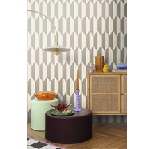 Interiér s geometrickou tapetou, stojacou lampou, komodou a dekoratívnymi predmetmi.