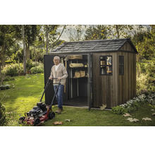 Muž s kosačkou na trávu pred záhradnou kôlňou s policami