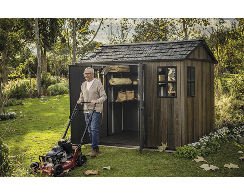 Muž s kosačkou na trávu pred záhradnou kôlňou s policami