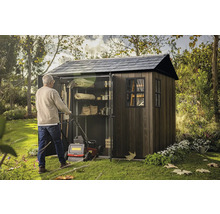 Muž tlačí kosačku do záhradnej skrine s policami na uloženie záhradného náradia