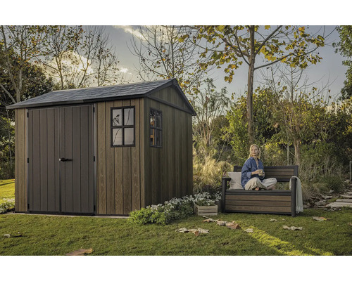 Záhradná scéna s dreveným záhradným domčekom a osobou sediacou na záhradnej lavičke