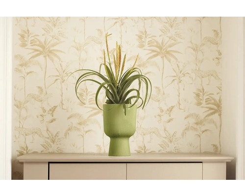 Dekoratívna umelá rastlina v rebrovanom kvetináči na komode pred vzorovanou tapetou