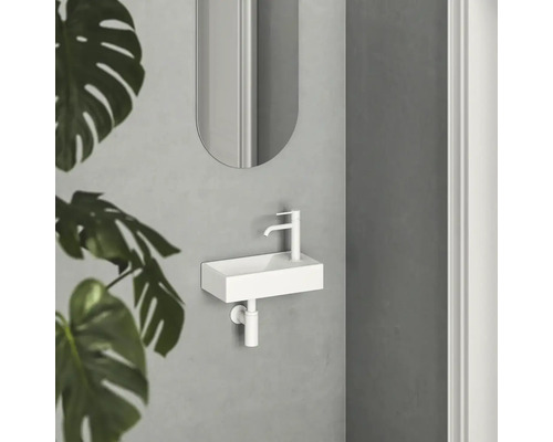 Malé biele umývadlo s batériou a zrkadlom v kúpeľni