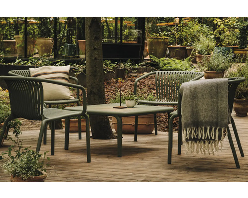 Záhradná scéna so stolom, stoličkami, vankúšom a dekou na terase obklopenej rastlinami