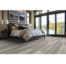 Spálňa s posteľou, nočným stolíkom, lampou a sivou drevenou podlahou