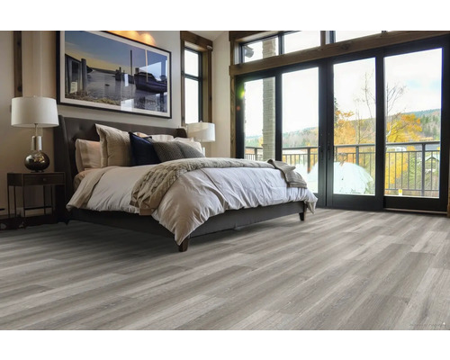 Spálňa s posteľou, nočným stolíkom, lampou a sivou drevenou podlahou