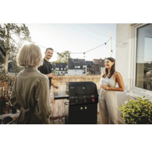 Scéna s plynovým grilom na balkóne, obklopená tromi hovoriacimi ľuďmi.