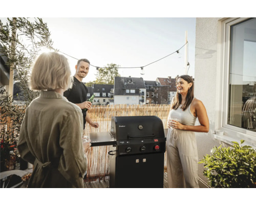 Scéna s plynovým grilom na balkóne, obklopená tromi hovoriacimi ľuďmi.