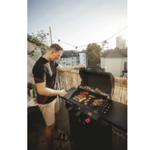 Muž griluje zeleninu a mäso na plynovom grile na balkóne.