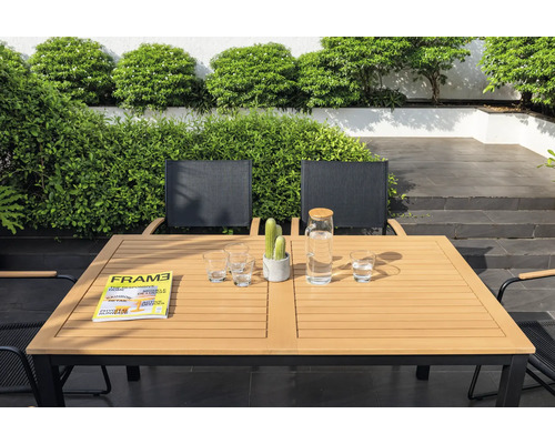 Záhradná scéna s jedálenským stolom, stoličkami, pohármi, karafou na vodu, časopisom a kaktusom