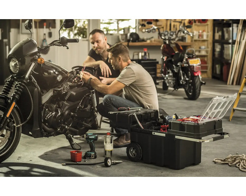 Dvaja muži opravujú motorku s bedňou na náradie v garáži.