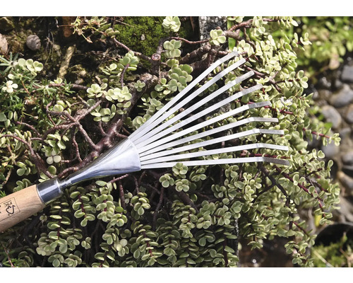 Kovové vejárovité hrable s drevenou rukoväťou pred zelenými rastlinami