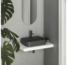 Moderná kúpeľňa s čiernym umývadlom na dosku, batériou a oválnym zrkadlom nad bielou policou.