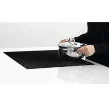 Indukčná varná doska s osobou, ktorá na ňu pokladá hrniec