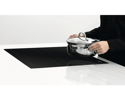 Indukčná varná doska s osobou, ktorá na ňu pokladá hrniec