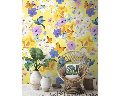 Dekoratívny interiér so žltou tapetou, zdobenou kvetmi, motýľmi a vtákmi, doplnený o prútené kreslo a izbové rastliny