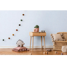 Svetlá detská izba s drevenou podlahou, dreveným stolom, ratanovým kreslom a dekoratívnymi prvkami, ako je girlanda, vankúše a rastlina.