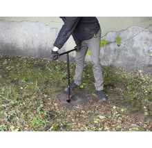 Osoba vŕta dieru do zeme pomocou zemného vrtáka.